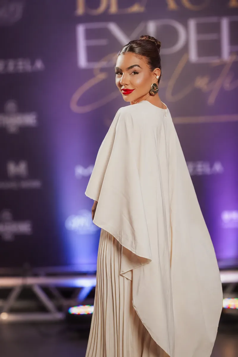 Dani Xavier de vestido creme com capa, sorrindo por cima do ombro em um evento